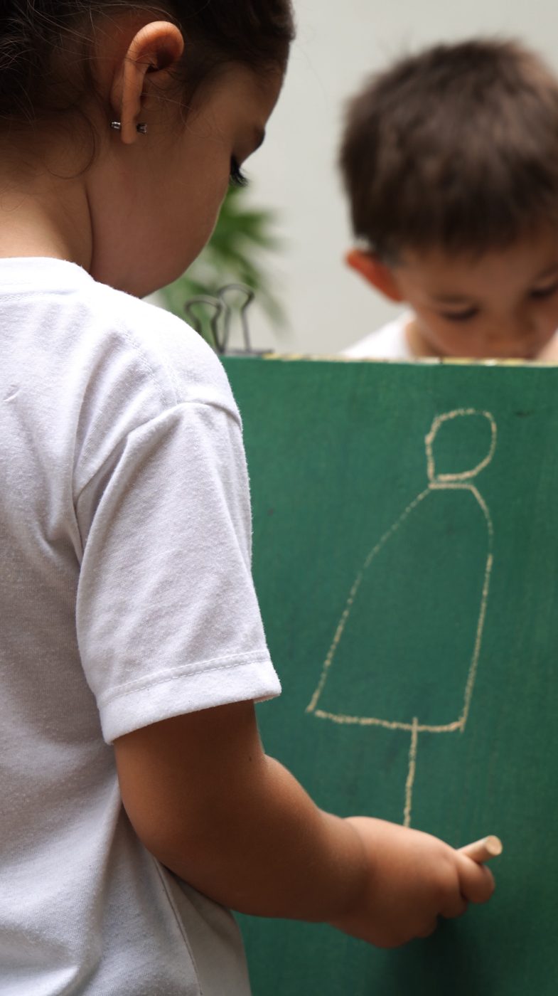 Una niña dibuja una figura con gis en una pizarra verde.