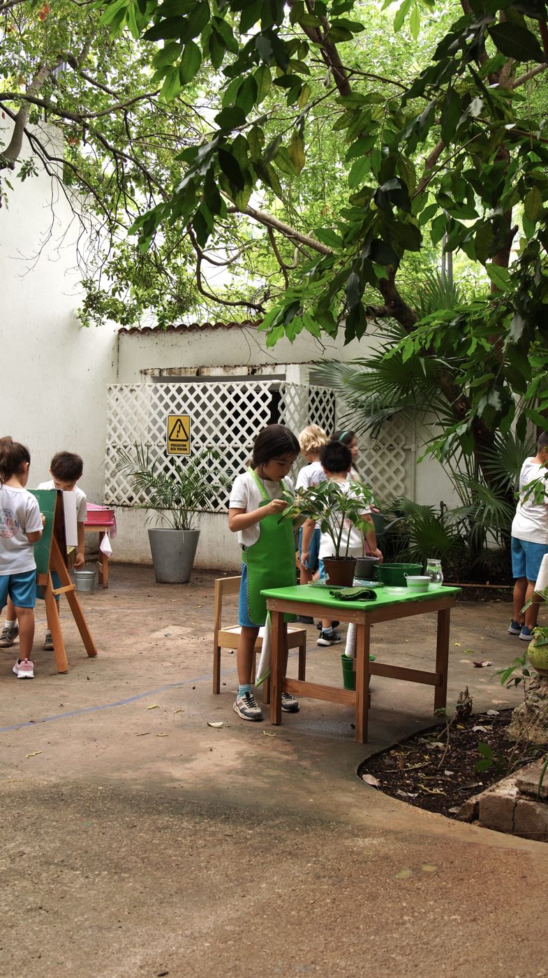 Una niña con delantal verde acomoda una planta en el patio.